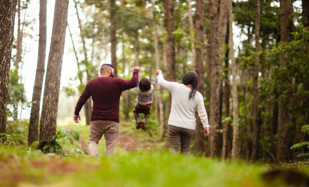 Man and a woman in a forest, swinging a small child between them